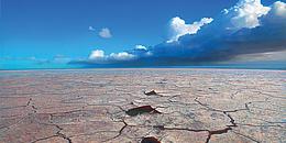 Gemälde einer Einöde mit tiefen Rissen im Boden; strahlend blauer Himmel mit Wolken