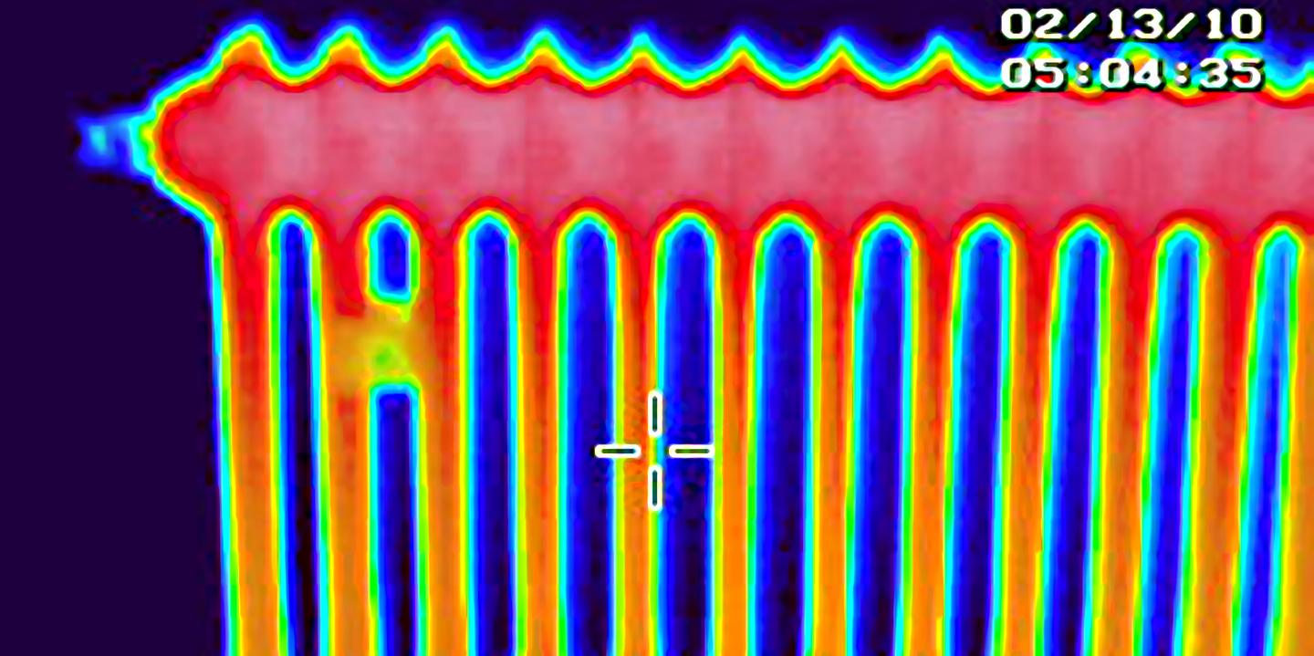 Infrarot-Wärmebild eines Zentraheizungskörpers. Dunkelblauer Hintergrund, die Zentralheizung ist oben rot, nach untengehend wird die Heizung gelb