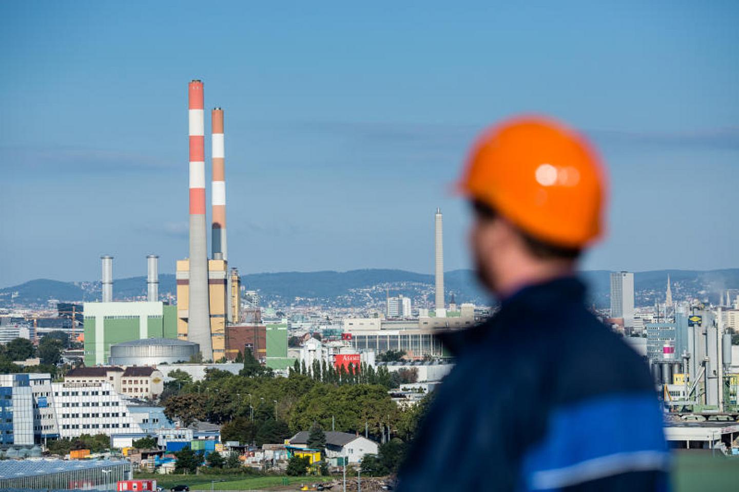 Blick auf das Kraftwerk Simmering Wien mit im Vordergrund stehender Arbeiter mit orangem Helm