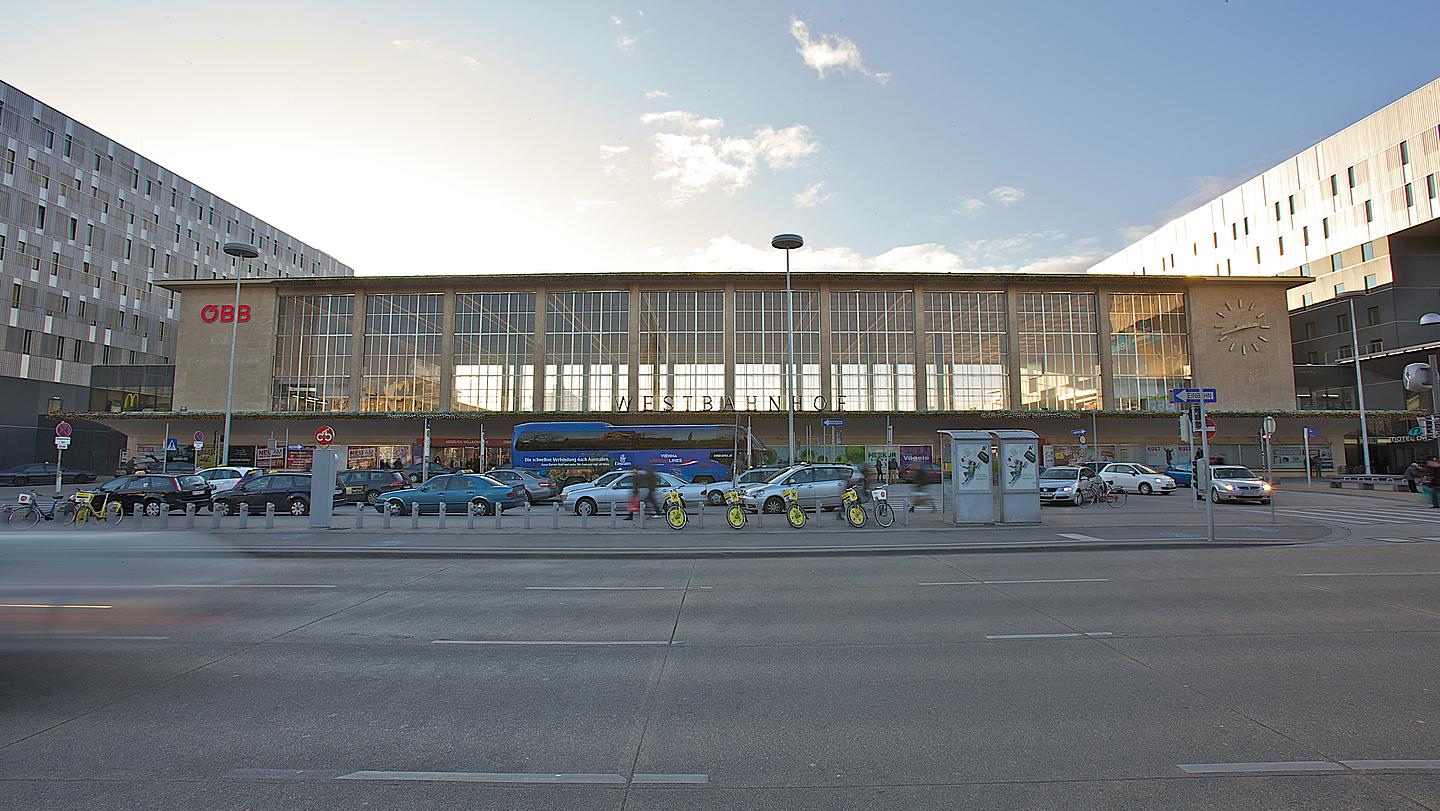 Außenansicht von der Bahnhofshalle des Westbahnhof Wiens, vom Europaplatz aus gesehen. Davor befindet sich eine City Bike Station und eine Bus- sowie Taxihaltestelle.