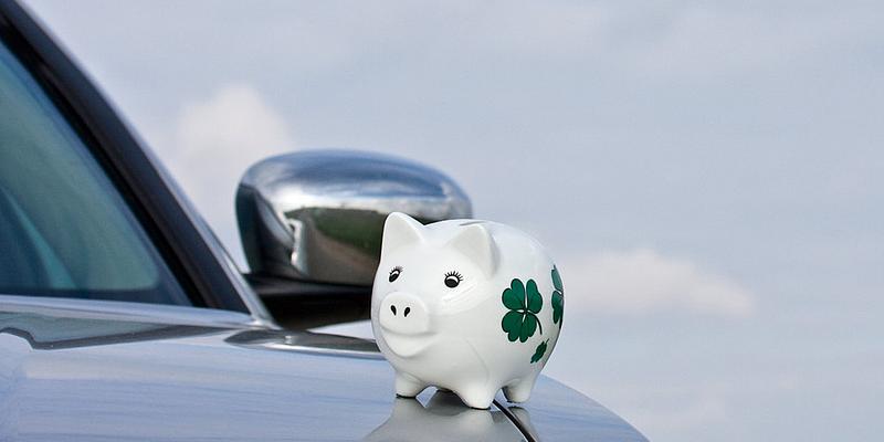 Weißes Sparschein sitzt auf Motorhaube von silberenem Auto.