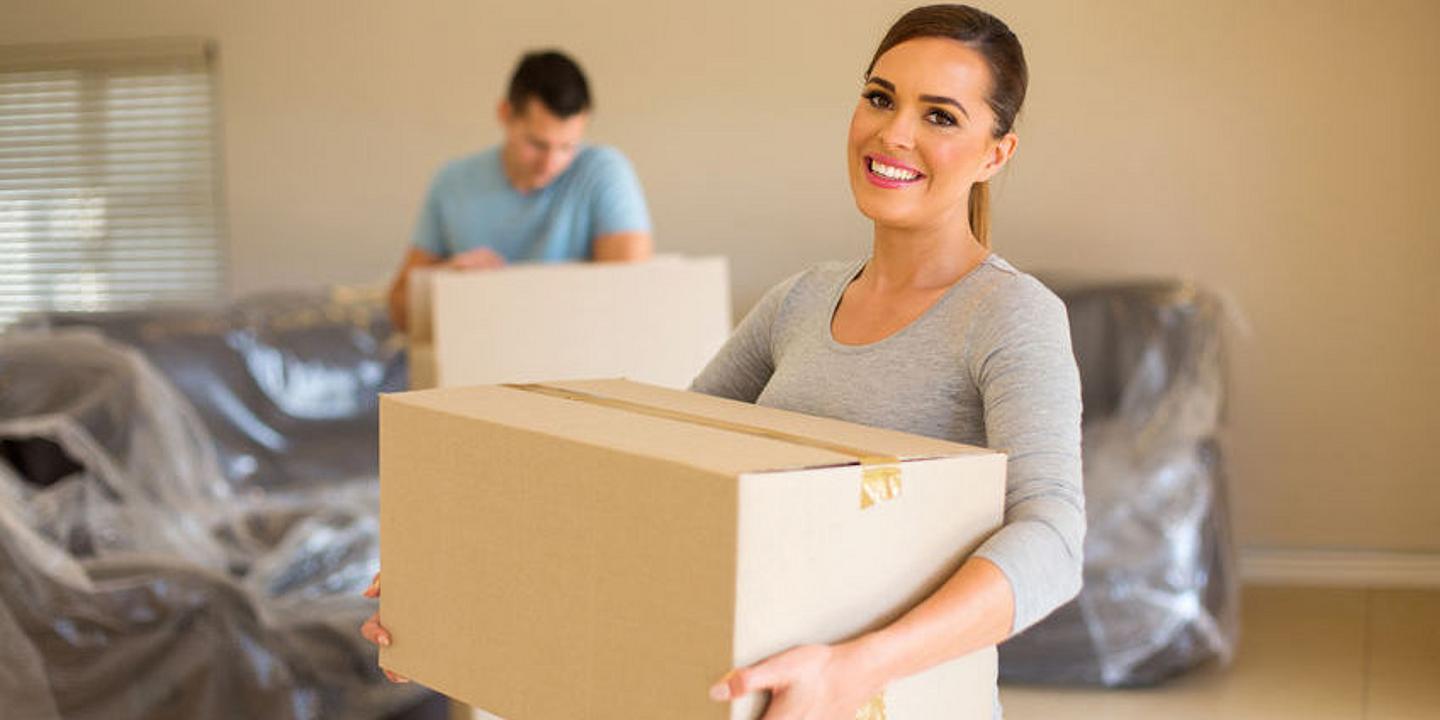 Eine Frau trägt Schachtel im Hintergrund verpackte Couch