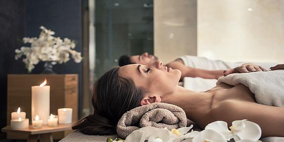 Eine Frau und ein Mann entspannen im Day Spa bei Kerzenschein auf Massageliegen.