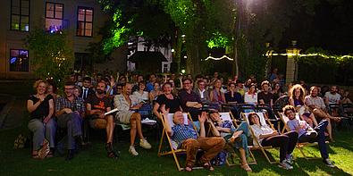 Menschen sitzen im Dunkeln in Strandstühlen und beobachten Film.