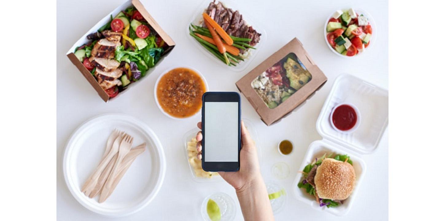 Essen das in Lieferboxen auf einem weißen Tisch liegt, Frau hält ein Smartphone darüber