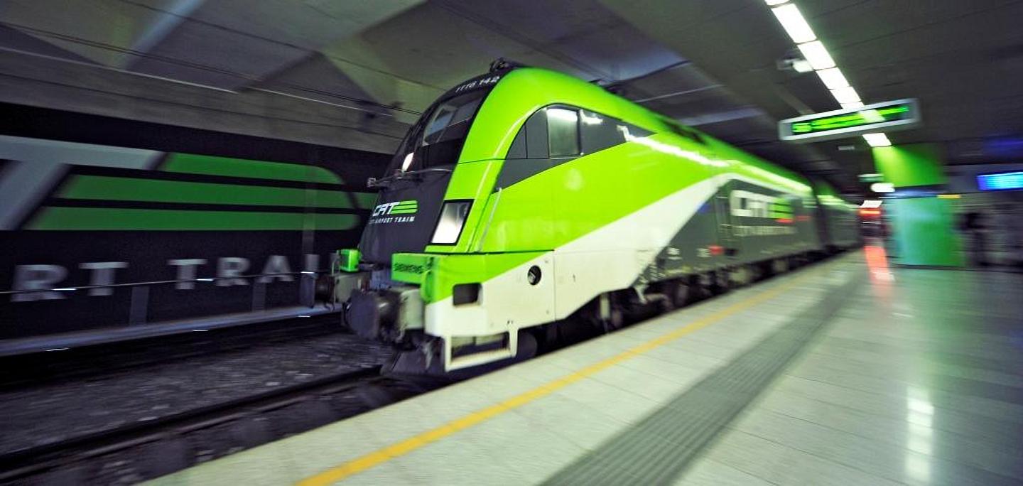 Dynamisches Bild eines einfahrenden City Airport Trains, kurz CAT, am menschenleeren Bahnsteig. Das grelle grün des Zuges steht in Kontrast mit der grauen Färbung der unterirdischen Station. Die Schrift der Anzeigetafel auf dem Bahnsteig ist verschwommen.