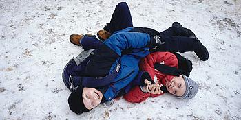 Zwei Jungs die im Skianzug im Schnee herumtollen