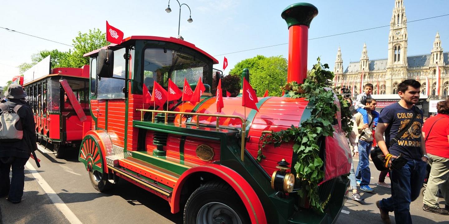 Rote Lilliputbahn mit SPÖ-Fahnen fährt vor dem Rathaus vorbei.