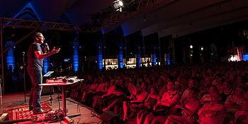 Kabarettist Gernot Krulis vor Publikum auf der Bühne im Rotlicht