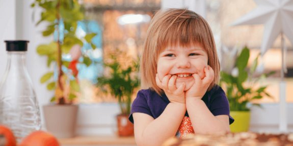 ein lächelndes Mädchen sitzt am Tisch und wartet auf ihr Essen