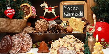 Ein schön angerichteter Weihnachtstisch mit Lebkuchen,Tannenzweigen und zapfen,Kerzen und Christbaumschmuck.Im Hintergrund eine kleine Tafel mit dem Gruß Frohe Weihnachten!