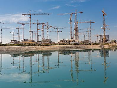 Viele Baukräne spiegeln sich im Wasser