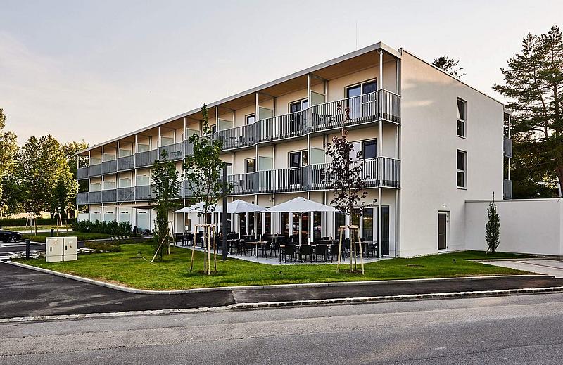 Weißes Hotel von Außen mit Wiese und Terrasse 