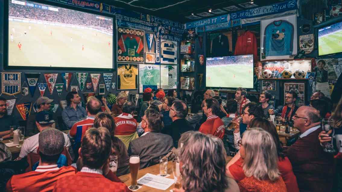 Menschen die gemeinsam in einer Bar auf einem Fernseher Sport schauen.