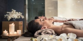 Eine Frau und ein Mann entspannen im Day Spa bei Kerzenschein auf Massageliegen.