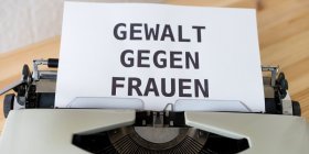 Das Bild zeigt ein Blatt in einer Schreibmaschine mit der Aufschrift "Gewalt gegen Frauen". 