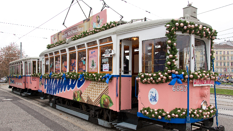 Eine Straßenbahn die weihnachtlich dekoriert ist und in Manner-Optik erstrahlt