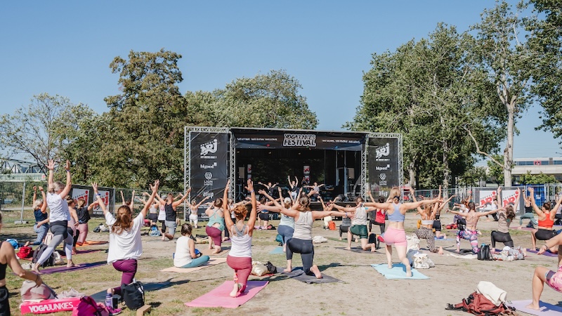 Eine Menschengruppe, die gemeinsam im Freien vor einer Bühne Yoga macht. 