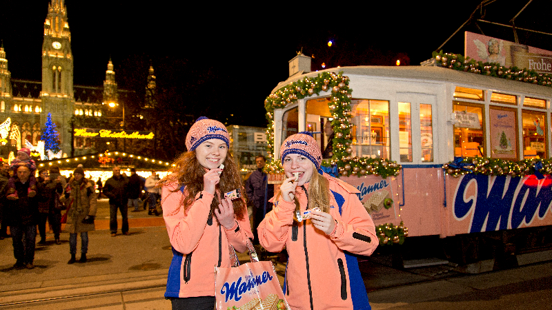 Zwei Mädels stehen vor der Manner-Weihnachtsbim und essen Manner-Schnitter