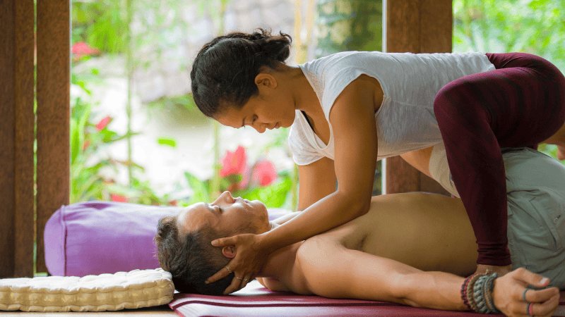 Ein Mann liegt am Boden und bekommt eine traditionelle Thai Massage von einer Masseurin